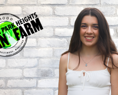 Sydney Santos Trainee Sydney Santos stands against brick wall next to logo for PPHUF