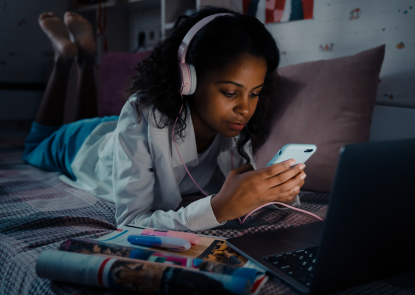 Teenager in bed looking at her phone with headphones on